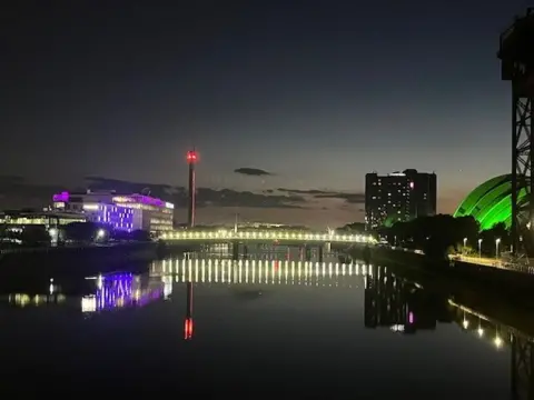 Ali Currie Buildings are lit green and purple in the distance, with the River Clyde stretching between them and going into the distance