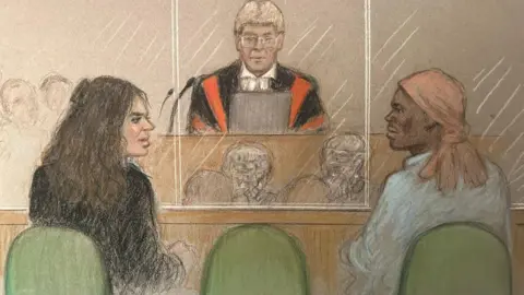 Julia Quenzler A court sketch showing Constance Marten, a woman with long brown hair wearing a dark top, and Mark Gordon, who has a peach-coloured headscarf and is wearing a shirt, looking at each other while sitting in a glass dock in court with the judge before them wearing a wig and red and black robes.