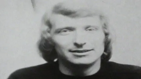 Gale Cleeland An archive black-and-white head-and-shoulders photograph shows a young man with shoulder-length light-coloured hair, wearing a dark top. The image is softly focused, with a plain light background and the subject facing towards the camera.