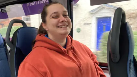 A woman wearing a red hoodie, sat on a bus.