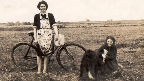 An Iodhlann A woman with a bike and a girl on the ground with a dog