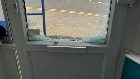 Supplied A close-up of a white door with a large broken window and a view out on to the street.