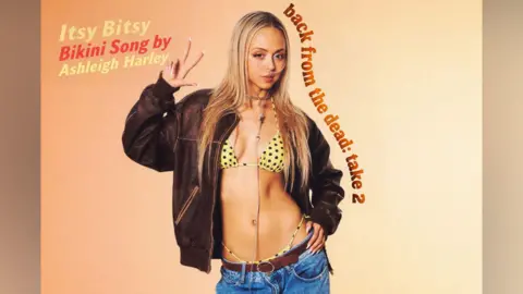 Suzanne Harley Harley, wearing a black leather jacket, a yellow bikini top and blue jeans, holds up a peace sign and places her other hand on her hip.