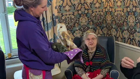 The Birches A woman in a purple top holds an owl while a female resident with glasses and a multi-coloured top watches