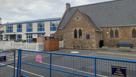 Castel Primary School with a blue fence in front of a playground with the school buildings behind