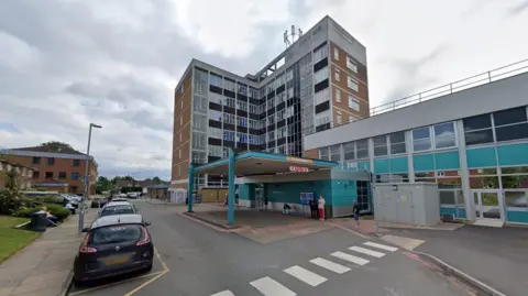 Google A large brown and beige building with dozens of windows. Cars and a zebra crossing can be seen in front.