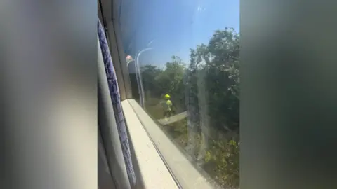 John Linington A photo looking out of the window of a train. A man in yellow helmet is stood next to the tracks.