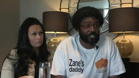 A woman and a man sat in a living room. The man is talking. 