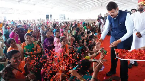 Sharad Badhe Devendra Fadnavis dressed in a blue jacket, white shirt and black trousers, greets women, as BJP workers spray flower petals on the crowd 