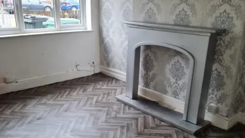 A living room with a grey fireplace and wallpaper, there is no other furniture in the room