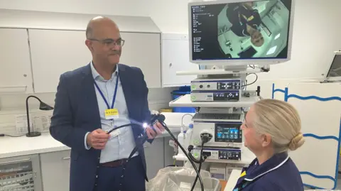 BBC Dr Sanjeev Pattni, a consultant Gastroenterologist and co-head of service at Leicestershire's Hospitals, showing a nurse the endoscopy equipment in a medical room.