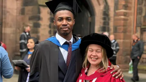 University of Chester Aaron Agbanu and Emma Moore pose together as students mills around outside the cathedral after the ceremony. They are wearing graduation hats and robes. 