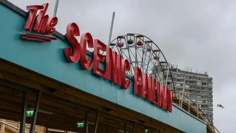 Getty Images Large red letters reading "The Scenic railway" on a blue roof. Part of a wooden rollercoaster, a ferris wheel, and a tower block can be seen in the background.