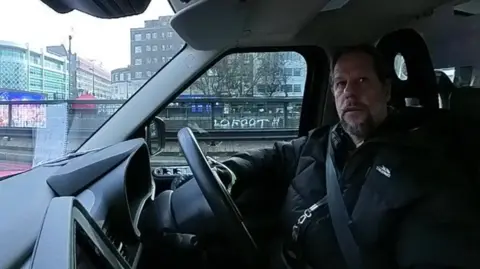 A cab driver sitting in his cab in traffic on the Euston Road