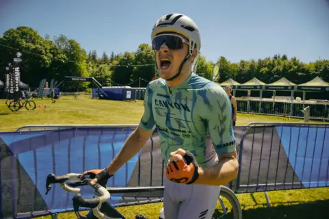 Red On Sports/Angus MacKinnnon A cyclist in a green top and dark glasses punches the air in celebration