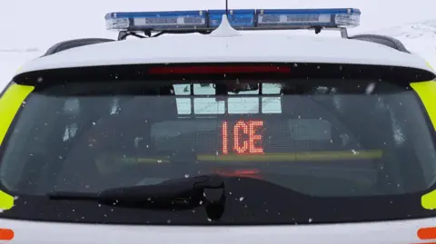 Back of a police car displaying the message 'ice' on a snowy day.