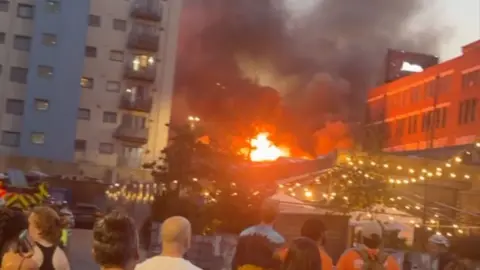 Large fire that can be seen from a square where people are stood watching it