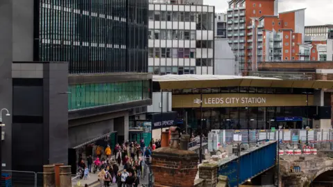General view of Leeds City Station, with passengers walking in front of the entrance.