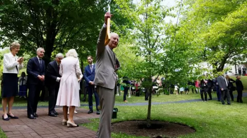 Reuters Britain's King Charles holds a shovel as he participates with Queen Camilla in a ceremonial tree planting next to Canada's Prime Minister Mark Carney as they visit the Rideau Hall residence during a two-day visit in Ottawa, Ontario, Canada May 26, 2025.