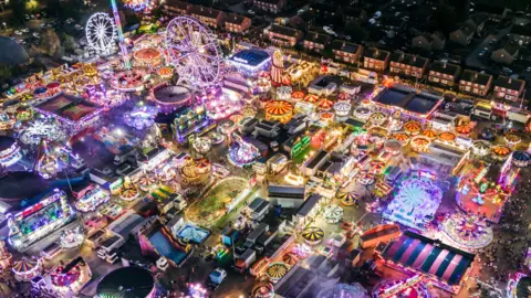 A drone view of Hull Fair at night, showing rides and stalls lit up in a wide range of colours.