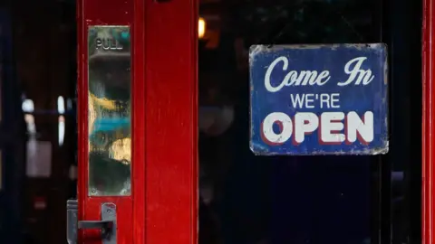 A red pub door with a 'Come in we're open' sign