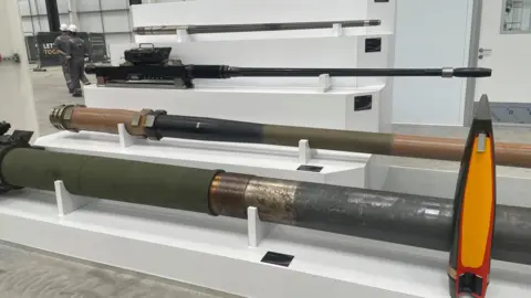Simon Thake A series of large weapons laid out in a white displace case