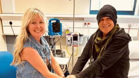 PA Media The Alarm singer Mike Peters holds hands with his wife Jules on his hospital bed