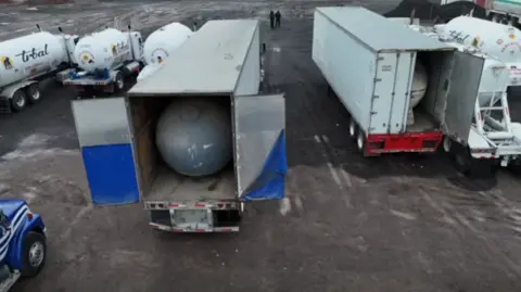 Stationary fuel tankers loaded up in white lorries inside a parking lot in the early hours of the morning