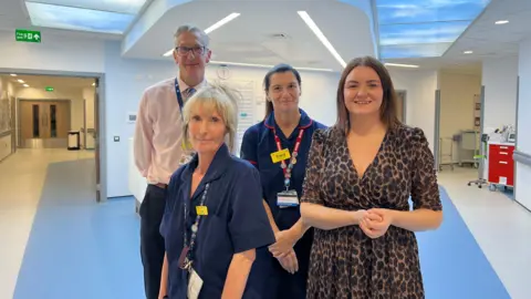 Dr Simon Constable and MP Leigh Ingham are stood with two nurses at the opening of the new day-case unit at County Hospital in Stafford. There is a corridor and nurses' station behind them.