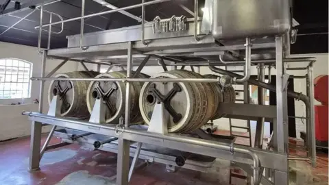 A stainless steel brewing mechanism involving six large barrels under metal equipment