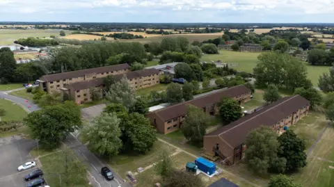 An aerial view of MDP Wethersfield, with four accommodation blocks visible and grass areas, with fields in the background.