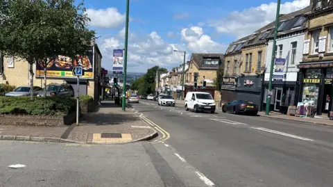 BBC An image of Leeds Road in Bradford, with a car park on the left side and traffic using both lanes on the right side of the photo. 