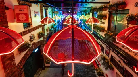 Different coloured umbrellas hanging on lines above a street.
