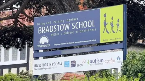 A dark blue sign reading BRADSTOW SCHOOL. It is among green hedges and trees