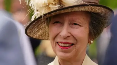 PA Media A close-up of Princess Anne smiling. She had short brown hair which is tucked under a brown hat.