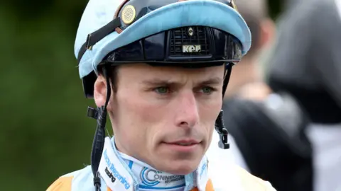 A close-up of a jockey wearing a helmet with a serious facial expression