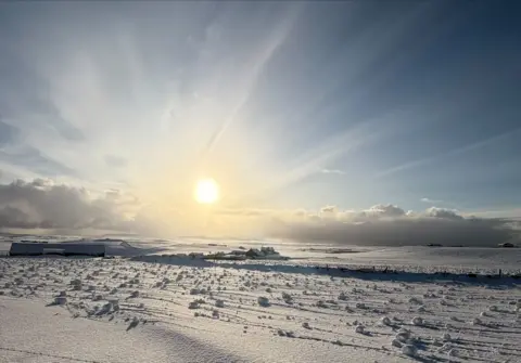 Steven Voy A snow-covered field under a bright blue sky. "Curls" of snow can be seen scattered across the landscape