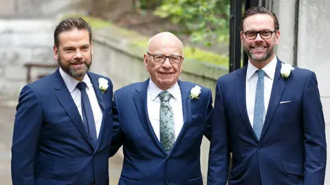 Getty Images Lachlan, Rupert and James Murdoch all wearing blue suits smiling at the camera at Rupert's wedding to Jerry Hall in 2016