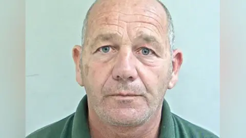Stephen Worden's mugshot. He has cropped white hair and stubble and is wearing a green polo shirt