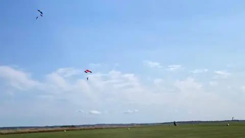 Landmarc Support Services Field with blue sky showing skydivers parachuting down to the ground.