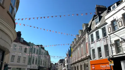 Bunting of flags strung across a Jersey shopping street with blue skies