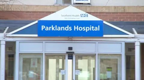 The entrance to Parklands Hospital. The name of the hospital is on a sign above white sliding doors.