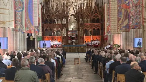 Crowds of people sat in Winchester Cathedral pews.