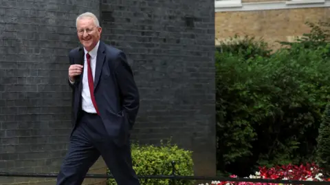 Reuters Hilary Benn walking into No 10 Downing Street. He has a smile on his face and he's wearing a suit and a red tie