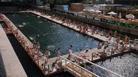 PA Media People relaxing at the 50m fresh-water pool Sea Lanes Canary Wharf, in London