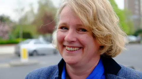 Richard Smith/BBC Vicky Ford, the former MP for Chelmsford, smiling at the camera. She is stood by the side of a road with traffic behind her. She is wearing a blue shirt and blue tweed jacket.