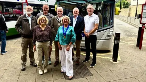 A group of men and women standing in front of a bus.