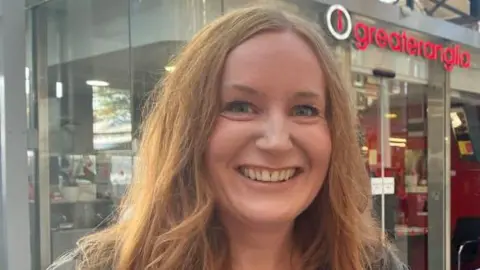 Andrew Turner/BBC Dawn McMullan, with auburn hair, standing near the Greater Anglia customer service office at Norwich Station