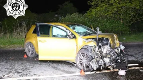 West Mercia Police The wreck of a yellow Volkswagen Golf car in the middle of a road.