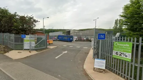 The entrance to Elland Recycling Centre, with a white arrow showing drivers the way in through a wide open gate, with a blue recycling bin in view beyond.